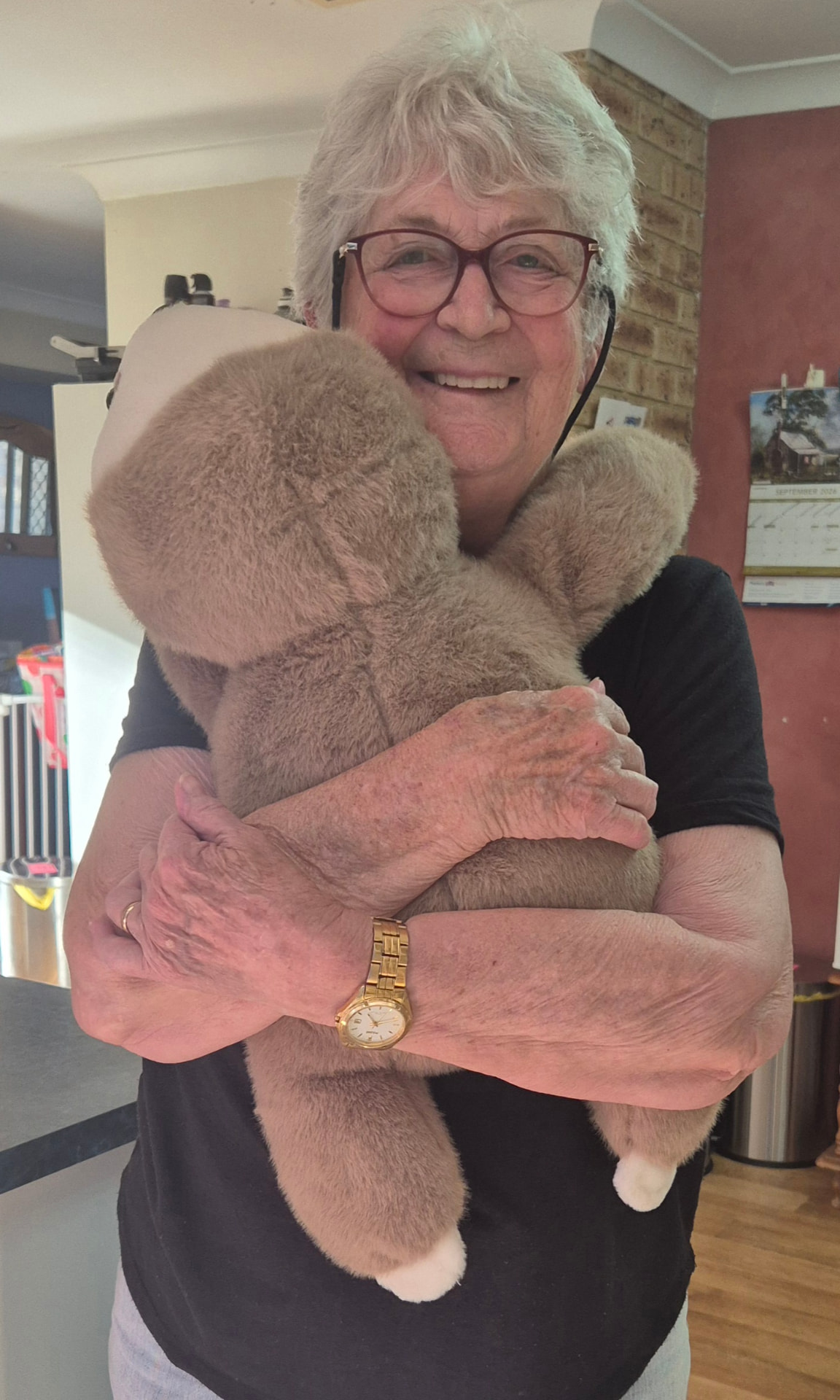 A smiling woman hugging the weighted sloth Sally close to her chest, its long arms wrapped around her