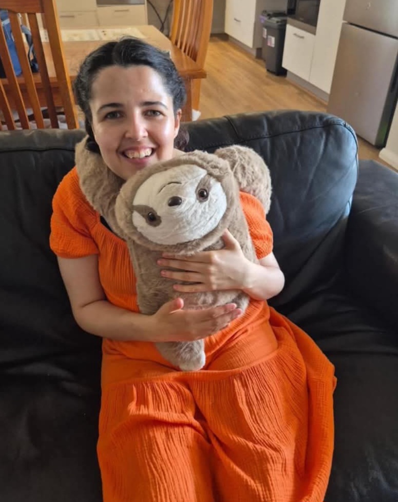 A smiling woman in an orange dress hugging the weighted sloth Sally on a lounge